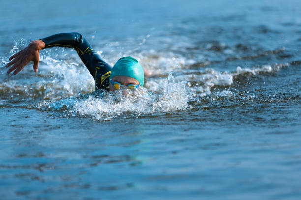 istock Professional triathlete swimming in river's open water. Man wearing swim equipment practicing triathlon on the beach in summer's day. 1331284032