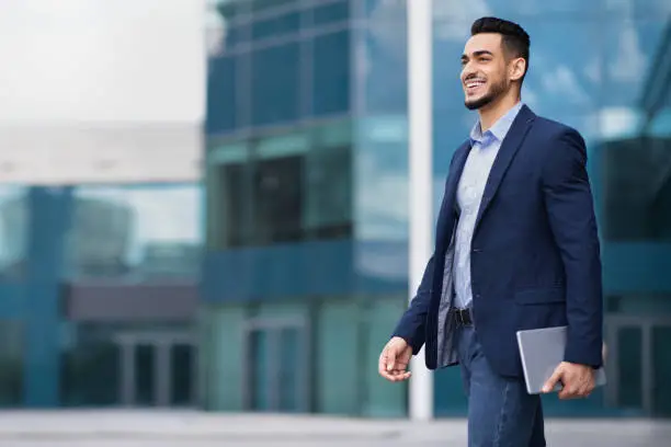 Photo of Happy young arab businessman walking from office, holding notepad