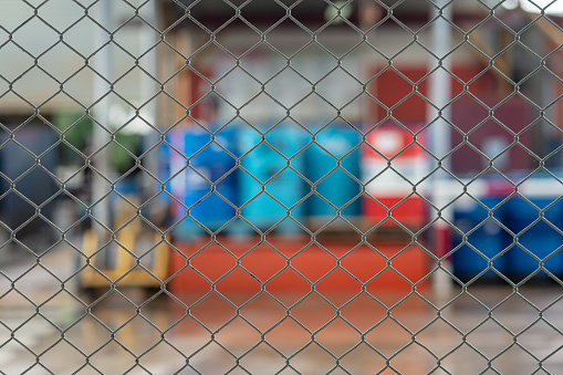 Metal wire fence with blurred background of chemical storage at the factory warehouse, Industrial workplace photo. Close-up and selective focus at foreground.