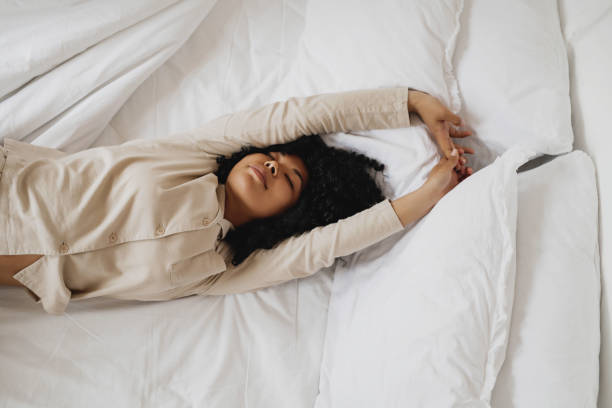 beautiful african american woman in pajamas waking up in her bed - wake up stretching women black imagens e fotografias de stock