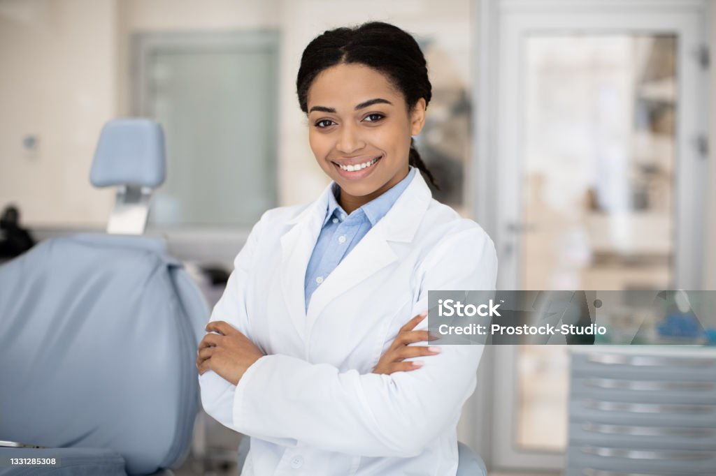 Female Dentist. Portrait Of Happy Black Stomatologist Woman Standing With Folded Arms Female Dentist. Portrait Of Happy Black Stomatologist Woman Standing With Folded Arms At Workplace In Modern Dental Clinic Interior, Professional Teeth Doctor Smiling And Looking At Camera, Closeup Dentist Stock Photo