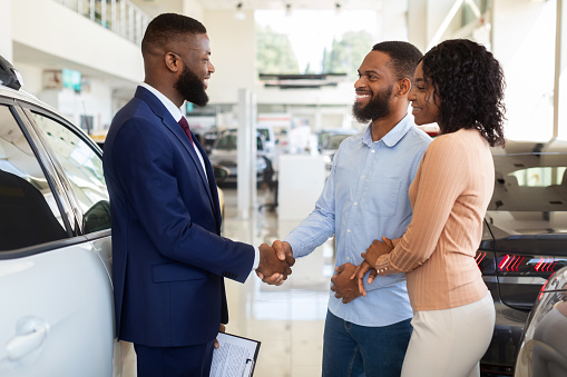 Sales Manager Helping Black Couple Choose New Car In Modern Dealership Center, Shaking Hands After Successful Deal, African American Spouses Buying Family Vehicle In Auto Showroom, Closeup