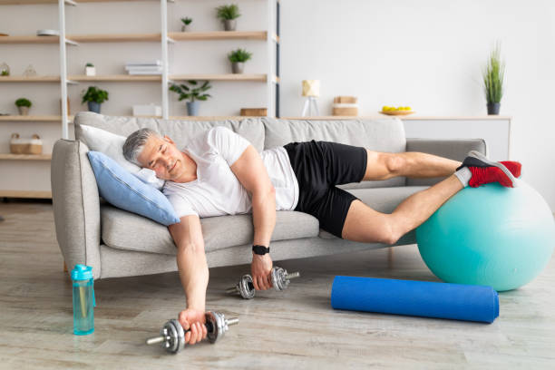 istock Exhausting home training. TIred mature man sleeping holding dumbbells, lying on sofa, resting after morning workout 1331285473