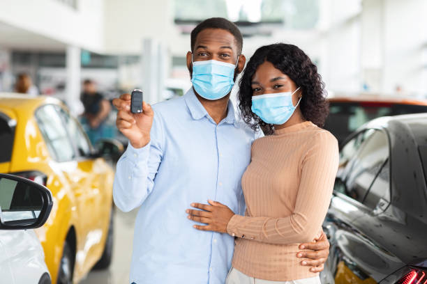 young african american spouses in medical masks demonstrating car key at camera - car old african descent car salesperson imagens e fotografias de stock