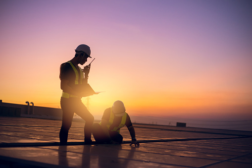 Dos técnicos reparan las células solares de mantenimiento preventivo anual en la fábrica de techo bajo la luz del sol de la mañana. photo
