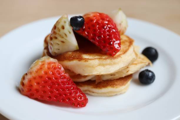 Pancakes with fresh strawberries and blueberries on top in white plate