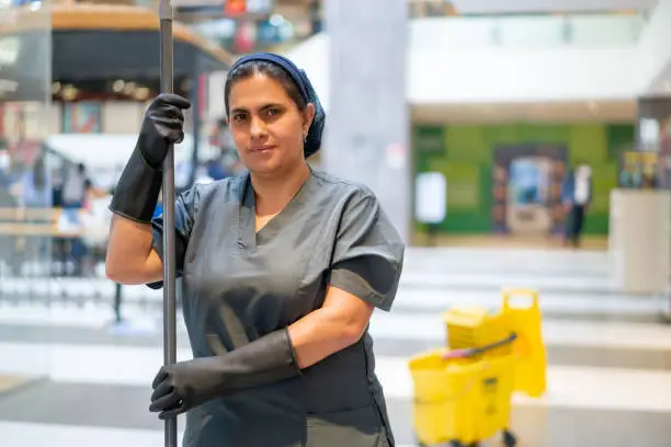 Portrait of a Latin American cleaning lady mopping the floor while working at a shopping mall and looking at the camera smiling