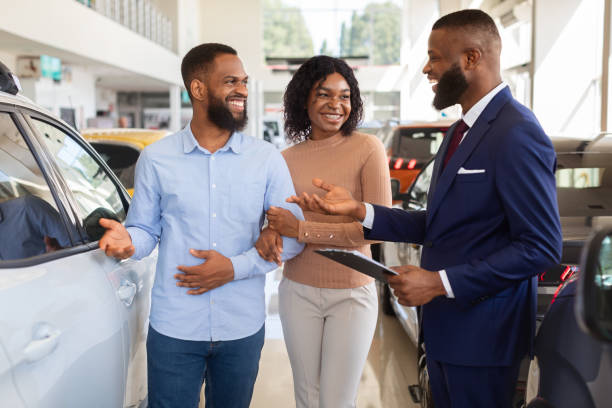 felice coppia nera che parla con il venditore mentre sceglie l'auto nel centro concessionario - car african descent shopping car dealership foto e immagini stock