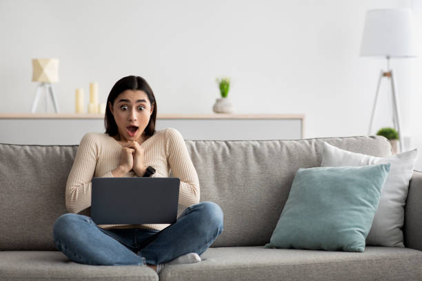 Surprised young arab lady gesturing on sofa at home Shocked business woman sitting in front of laptop looking at screen. Funny facial expression emotions, feelings, problems perception, reaction. Surprised young arab lady gesturing on sofa at home shocked computer stock pictures, royalty-free photos & images
