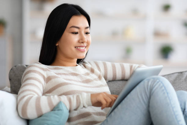 istock Young Asian Female With Digital Tablet Relaxing On Sofa At Home 1331288584