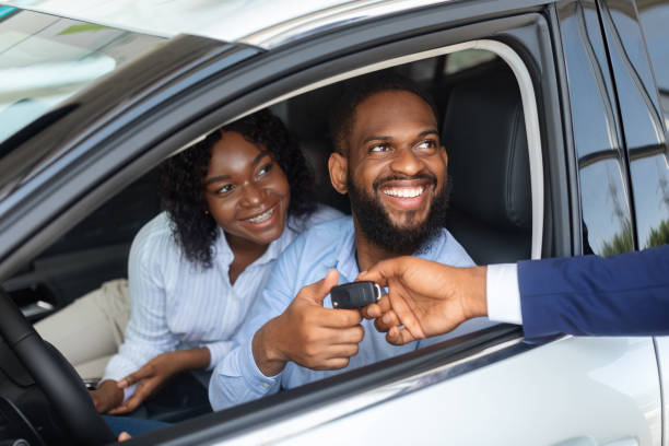 felice coppia afroamericana prendendo chiave dal venditore dopo aver acquistato nuova auto - car african descent shopping car dealership foto e immagini stock