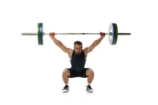 Full length portrait of man in sportswear exercising with a weight isolated on white background. Fit young muscular caucasian model with barbell training at abstract gym. Sport, weightlifting concept