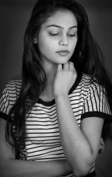 Photo of Black and white ortrait of a sad young woman in striped top contemplating with a blank expression.