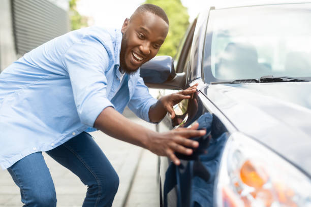 glücklicher afroamerikaner, der sein neues auto berührt - new automobile stock-fotos und bilder