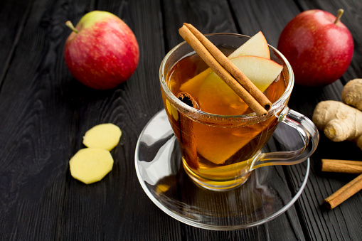 Hot tea with apple, cinnamon  and ginger in the glass cup on the black  wooden background. Close-up. Healthy drink.