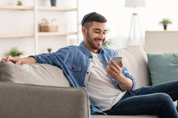 istock Smiling jew man using cellphone sitting on comfy couch 1331293871