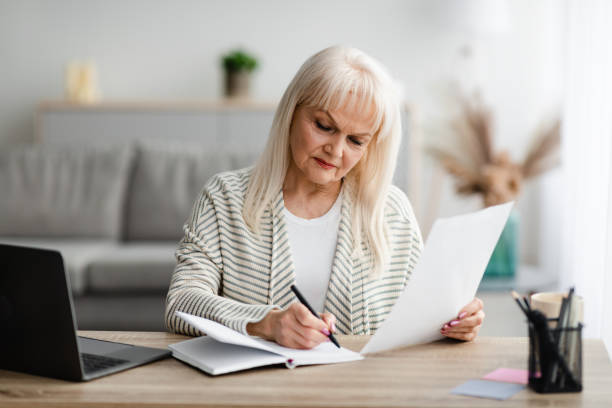 istock Focused mature woman writing and holding document at home 1331294022
