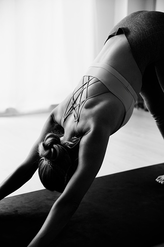 Detail of a woman`s back in a yoga asana. She is practicing Adho Mukha Shvanasana pose. Black and white photography.