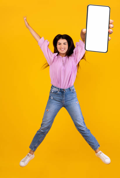 istock Overjoyed armenian lady holding smartphone, showing blank screen, jumping up over yellow studio background 1331296121