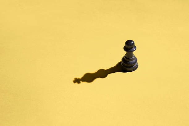 istock Black pawn with kings shadow on yellow background 1331296641
