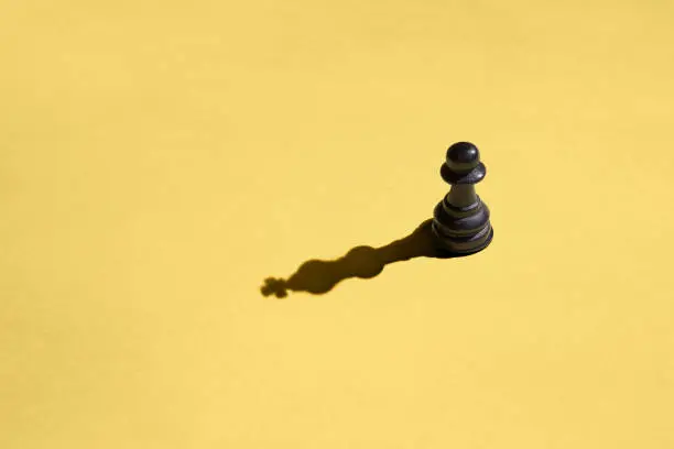 Photo of Black pawn with kings shadow on yellow background