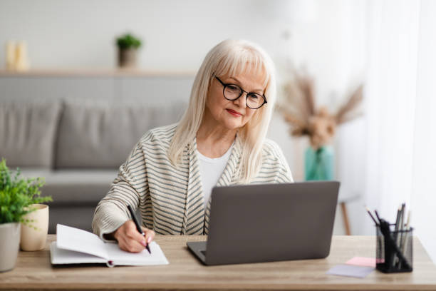 istock Mature woman writing and using laptop at home 1331296775