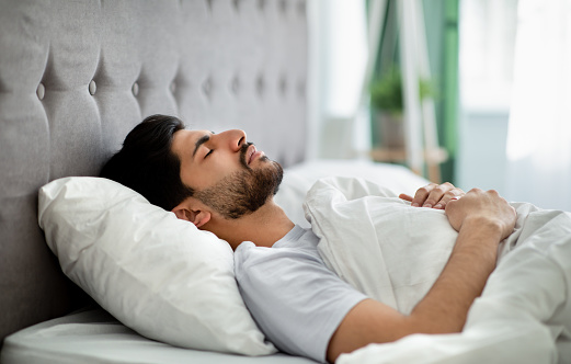 Deep male sleep. Young arab guy sleeping peacefully in his comfortable bed at home, lying with closed eyes on back. Recreation, time to rest and nap concept