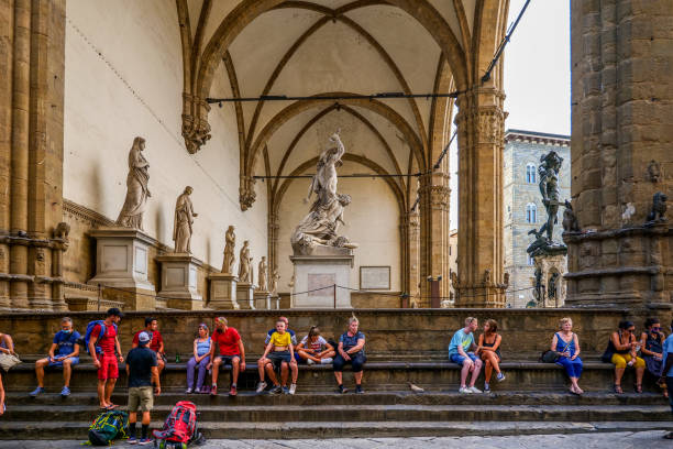 einige touristen ruhen sich unter der loggia dei lanzi auf der piazza della signoria im herzen von florenz aus - palazzo vecchio piazza della signoria florence italy italy stock-fotos und bilder