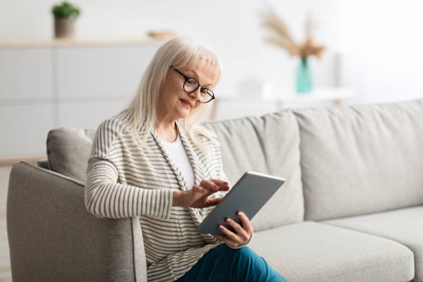 istock Mature lady in glasses using digital tablet sitting on couch 1331297971