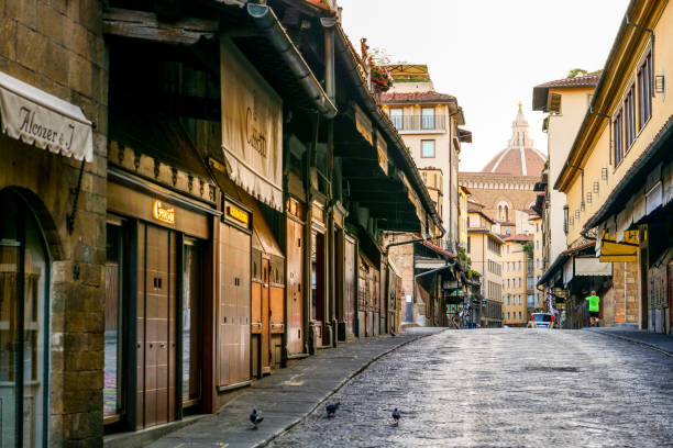 the early morning light reflects on the artisan goldsmith shops along ponte vecchio in the historic heart of florence - paving stone cobblestone road old imagens e fotografias de stock