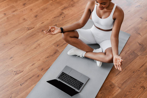 istock Black woman sitting on lotus position on mat with pc 1331298277