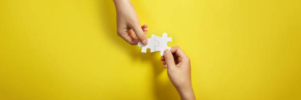 Two hand joining two matching puzzle pieces together in a conceptual image of teamwork and cooperation. stock photo