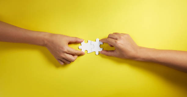 Two hand joining two matching puzzle pieces together in a conceptual image of teamwork and cooperation. stock photo