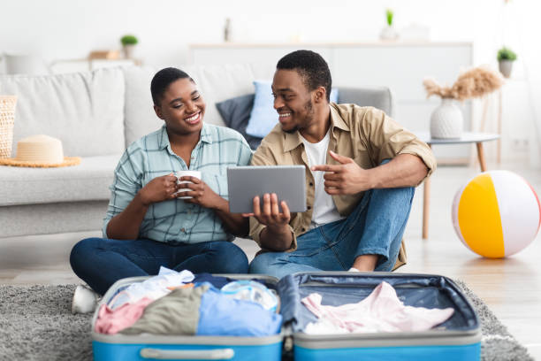 istock Black Tourists Couple Using Tablet Booking Tickets Packing Suitcase Indoors 1331301437