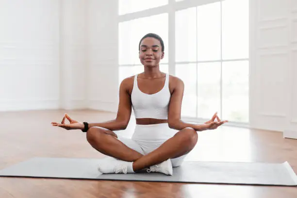 Photo of Young black woman sitting in lotus position on mat, meditating