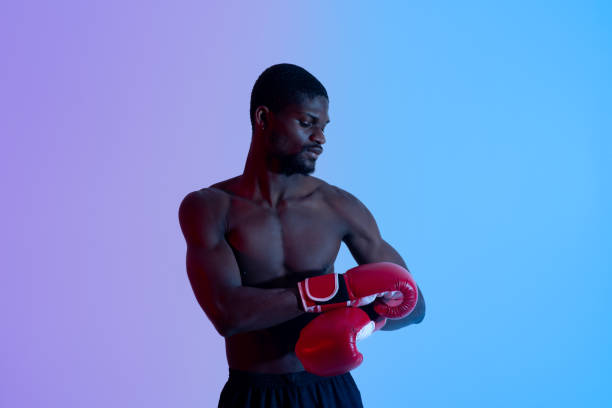 istock Professional young black boxer with bare torso putting on or taking off red gloves in neon lighting 1331301776