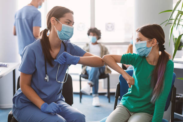 Teen Girl In Medical Mask Bumping Elbows Meeting Female Doctor Elbow Bump Greeting. Teen Girl In Medical Mask Bumping Elbows Meeting Nurse Doctor In Hospital Indoor. Social Distancing And Keeping Safe Distance For Covid-19 Protection Concept doctor head stock pictures, royalty-free photos & images