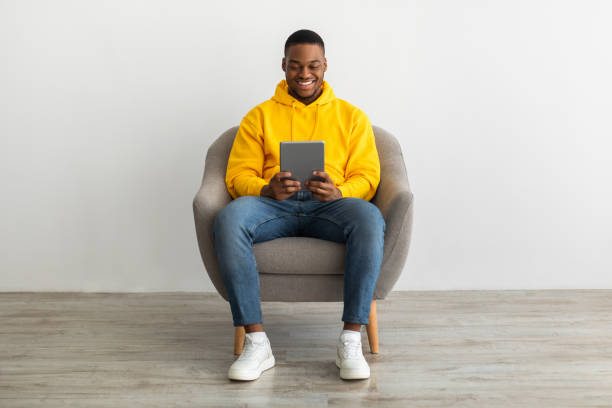 istock Positive Black Man Using Tablet Sitting Near Gray Wall Indoors 1331302743