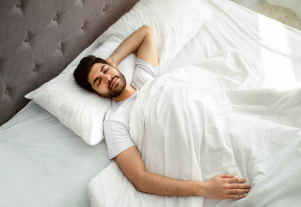 istock Arab guy sleeping resting peacefully in his comfortable bed at home, lying with closed eyes, above view 1331302816