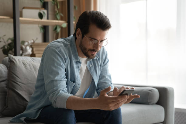 istock Man in glasses sit on sofa holding smartphone read messages 1331304114