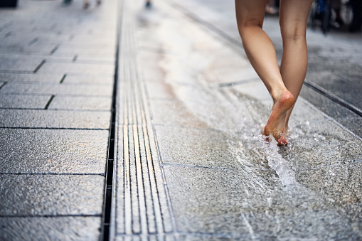 Teenage girl walking in water running from the fountain on the street