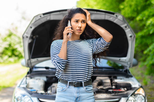 Nervous woman with open car hood calling auto service Nervous young woman standing by open car hood and calling to auto service, got broken at highway on a way to countryside. Female drive having phone conversation with friends, asking for help with auto beat up car stock pictures, royalty-free photos & images