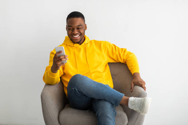istock Cheerful Black Man Using Cellphone Sitting Over Gray Wall Indoors 1331306823