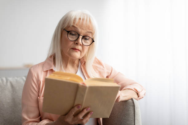 istock Focused mature woman in glasses reading book 1331307075