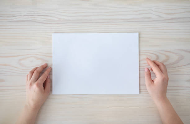 istock Female hands with white blank paper sheet on wooden table background, top view, empty space, flat lay 1331311775