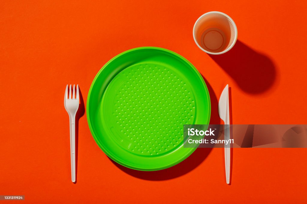 Plastic set of disposable tableware consisting of a plate, knife, cup and fork on an orange background. Environmental concept. Ban single use plastic. Plastic set of disposable tableware consisting of a plate, knife, cup and fork on an orange background. Environmental concept. Ban single use plastic. Top view. Blue Stock Photo
