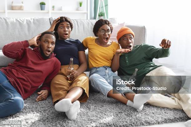 Shocked African American Friends Watching Horror Movie Sitting On Floor Stock Photo - Download Image Now