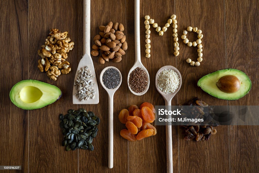 Healthy meal Wooden spoons with healthy seeds, nuts and dried fruits and word Mg arranged on wooden table Avocado Stock Photo