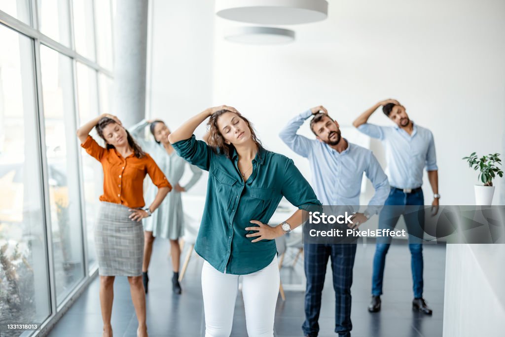 Stretching Exercise At Workplace Diverse colleagues doing neck stretching exercise standing in office. Multiethnic young office employees do workout exercises during break at work Wellbeing Stock Photo