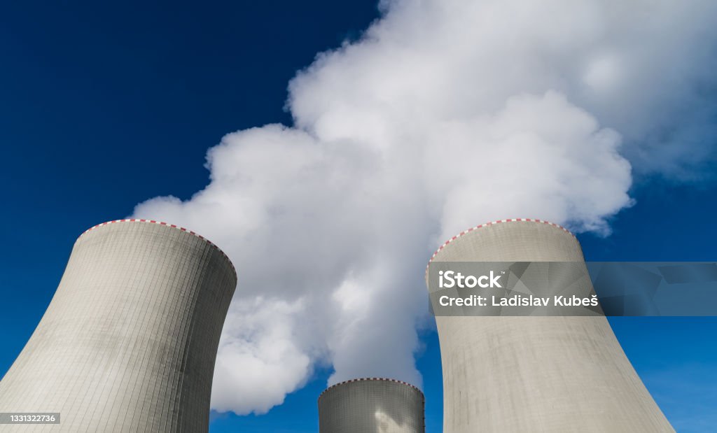 Closeup of nuclear power plant cooling towers belching out white plume of water vapor Top detail of large concrete structures removing heat from modern generating station on blue sky background. Ecology Nuclear Power Station Stock Photo